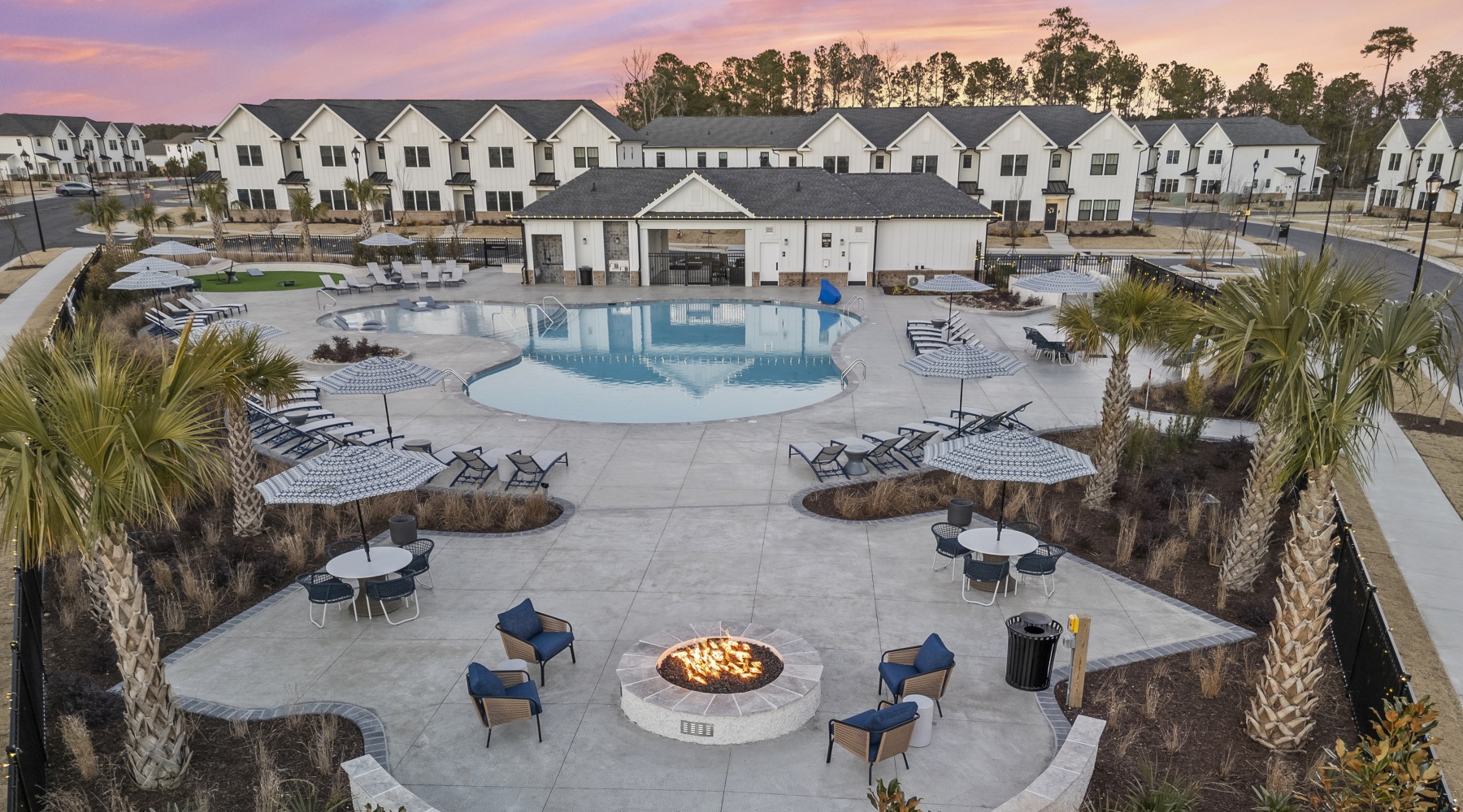 Outdoor clubhouse aerial view  A fire pit is surrounded by chairs and tables in a courtyard with a pool behind it.