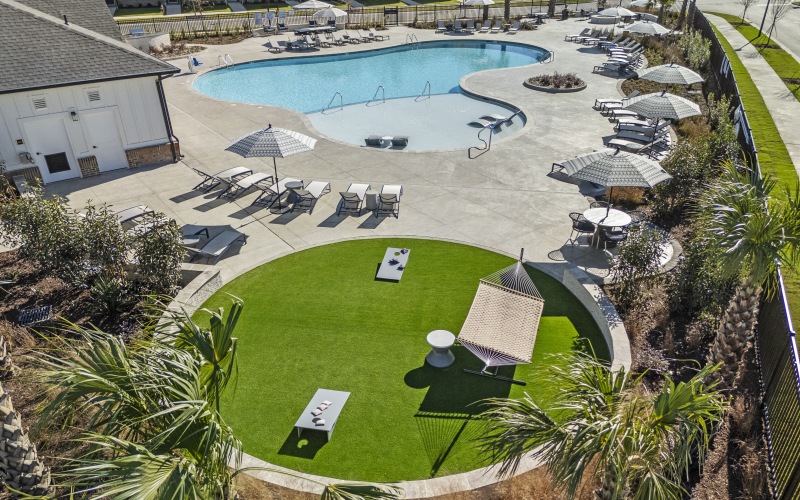 A grassy area with a hammock and a pool behind it.
